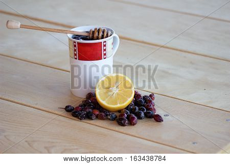 warm rose-hip tea with honey red and white mug dried rosehips whole and crushed half a lemon and everything resting on a wooden table