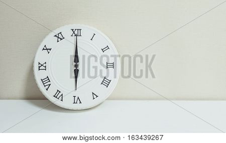 Closeup white clock for decoration at 6 o'clock on white wood desk and cream wallpaper textured background with copy space