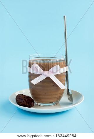 Homemade Banana Almond Milk and Espresso Smoothie with Medjool Dates in a glass with pink bow on pale blue background. A drinking spoon and a medjool date on a white saucer.