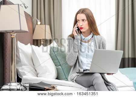 Displeased business woman calling with phone in the luxury hotel room. Staying at the hotel during the business trip