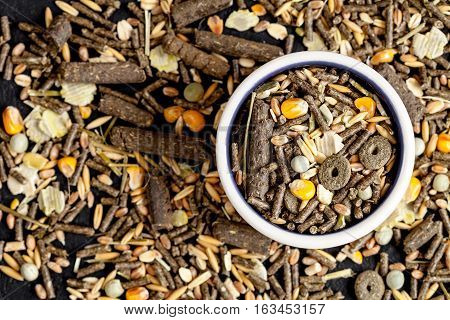 dry food for rodents in bowl on dark background top view.