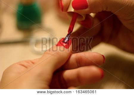hands of a young woman who paints her nails red and green nail polish