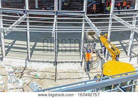 Excavator is moving over building site with raised up back bucket a self leveling power trowel machine is hanging sander for smoothing surface to finish concrete slab.