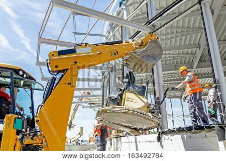 Zrenjanin Vojvodina Serbia - July 28 2015: Excavator is moving over building site with raised up back bucket a self leveling power trowel machine is hanging sander for smoothing surface to finish concrete slab.