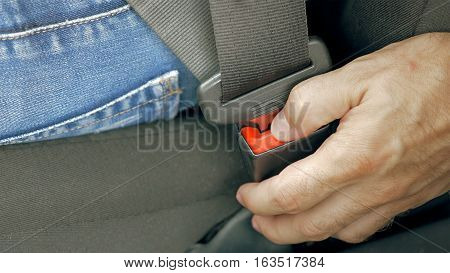 Close up of male hand unfastening releasing car safety seat belt while sitting inside of vehicle before driving. Safe travel is one of great importance on the road