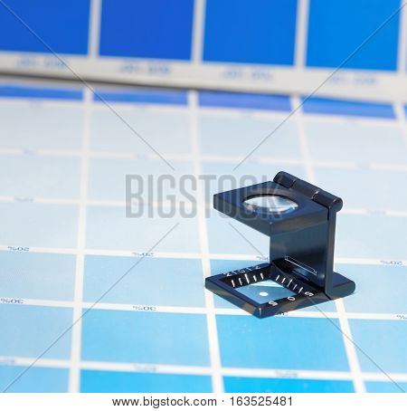 Magnifier or printer's loupe sits on a cyan test sheet in a pre-press workshop