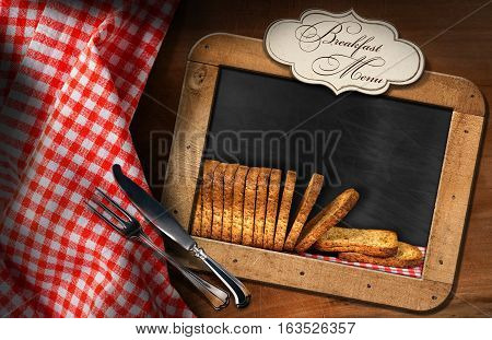 Rusks of wholemeal flour in a blackboard with a label with text Breakfast Menu. On a table with a checkered tablecloth and silver cutlery