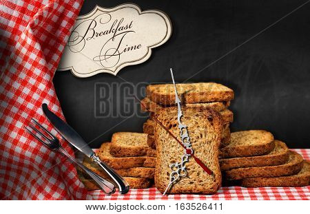Rusks on a table with a clock made with a rusk silver cutlery and a label with text Breakfast time