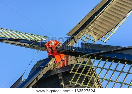 Closeup of a red painted windmill cross with sails against a blue sky. The hollow post mill was built in 1700.