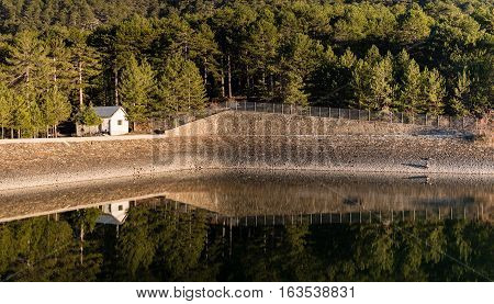 Small house and trees reflected on the damn. Prodormos Dam Troodos Cyprus.