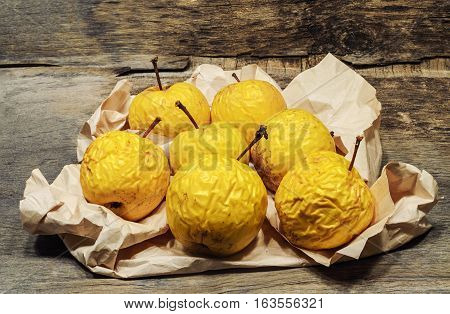shriveled yellow apples on crumpled paper. Wooden background