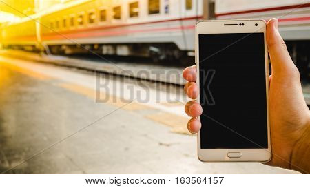 Hand holding blank smartphone screen for text with train station or railway station for background.
