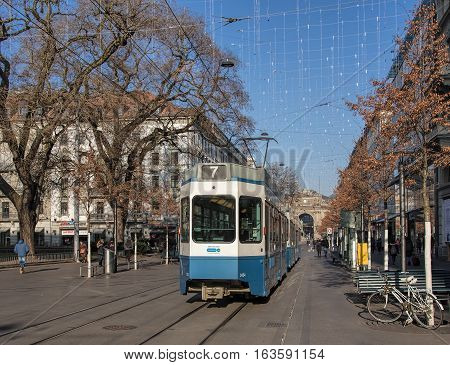 Zurich, Switzerland - 1 January, 2017: a tram passing along Bahnhofstrasse street, people on the street, lamps of the Christmas illumination above it. Bahnhofstrasse is Zurich's main downtown street.