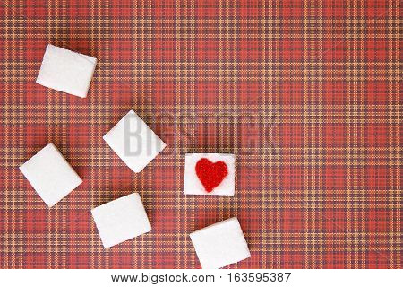 Sugar cubes with a red heart on one of them as background. Top view. Diet unhealty sweet addiction concept