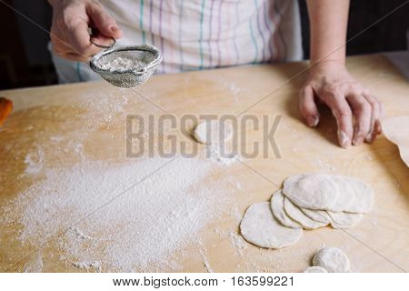 Close-up front view of two woman's hands sprinkle with flour dough for meat dumplings.