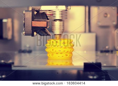 3D printer prints from the plastic figure closeup. 3D printer makes yellow model close-up on gray flat surface