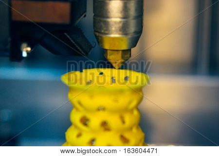 3D printer prints from the plastic figure closeup. 3D printer makes yellow model close-up on gray flat surface