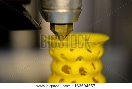 3D printer prints from the plastic figure closeup. 3D printer makes yellow model close-up on gray flat surface