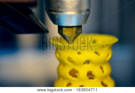3D printer prints from the plastic figure closeup. 3D printer makes yellow model close-up on gray flat surface