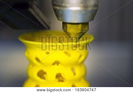 3D printer prints from the plastic figure closeup. 3D printer makes yellow model close-up on gray flat surface