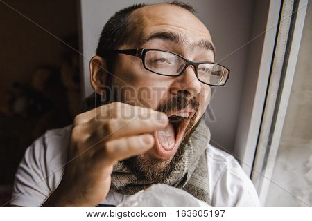 Young man blowing his nose while sitting at the window