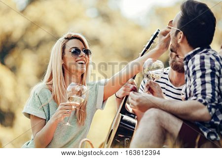 Happy young friends having picnic in the park.They are all happyhaving funsmiling and playing guitar.