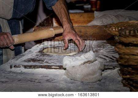 Man dressed in period clothes rolls the dough with rolling pin hands close-up in Nazareth Village Israel