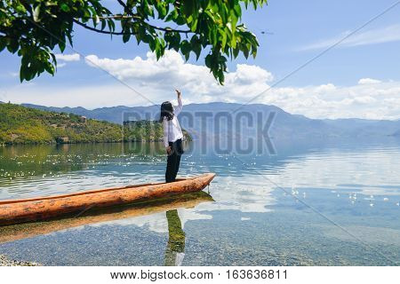 Single young Chinese woman looking up to sun, standing on boat by the bank of Lugu lake, Lijiang, China