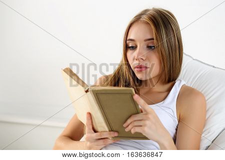 Young beautiful blonde woman lying in bed reading old book before or after sleeping. Hobby favourite literature reading for examination education work in bed reference book concept