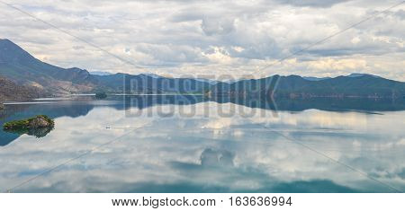 Single boat travels on mirror-like water at  Lugu Lake, Lijiang, China
