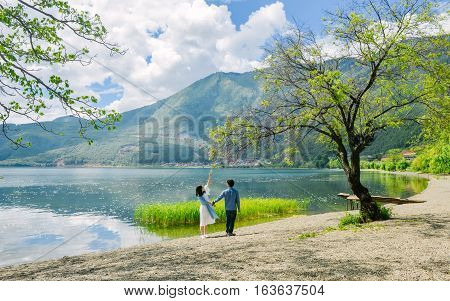 Young Chinese couple having fun while walking along the bank of Lugu lake hand in hand, at Daluoshui village, Lijiang, China
