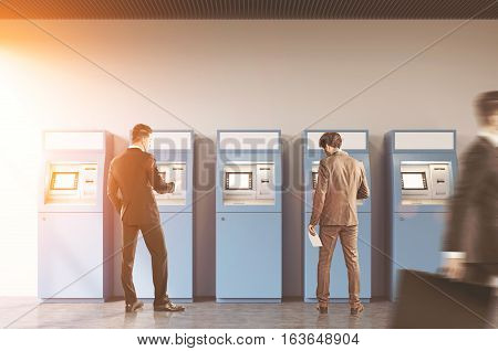 Hallway of an office or a bank. A man is rushing by. Two businessmen are standing near ATM machines. There is a cityscape on the foreground. Toned image.