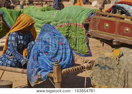 NAGAUR, RAJASTHAN, INDIA - FEBRUARY 15, 2008: Women in brightly coloured clothing sitting on a bed, known as a charpoy, at the annual livestock fair in Nagaur, India.