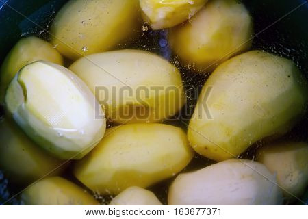 Peeled potato tubers are prepared for cooking. Whole potatoes in water