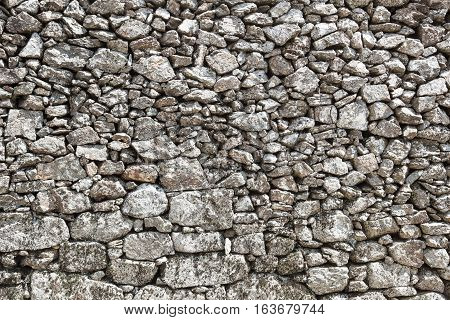 Outdoor stone wall in local stone, retaining wall of stone, background large stone boulders