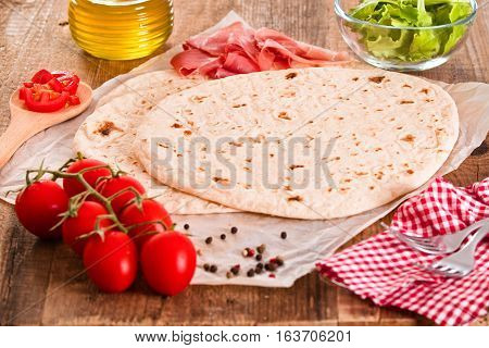 Piadina with ham and lettuce on baking paper.