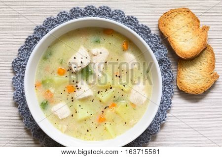 Chicken and potato chowder soup with green bell pepper and carrot in bowl with toasted bread slices on the side photographed overhead with natural light (Selective Focus Focus on the top of the soup)