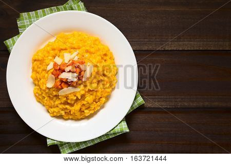 Fresh homemade carrot risotto made with pureed carrot garnished with roasted carrot and hard cheese photographed overhead on dark wood with natural light (Selective Focus Focus on the risotto)