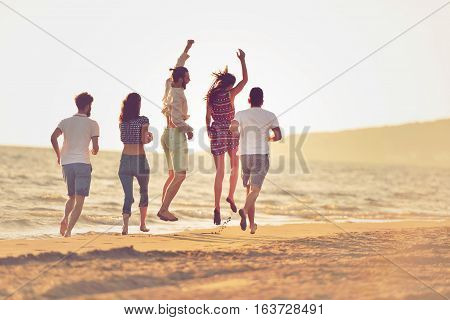 happy young people group have fun white running and jumping on beacz at sunset time.