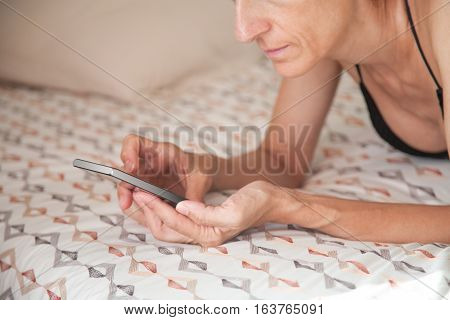 Smartphone In Woman Hands Lying On The Bed