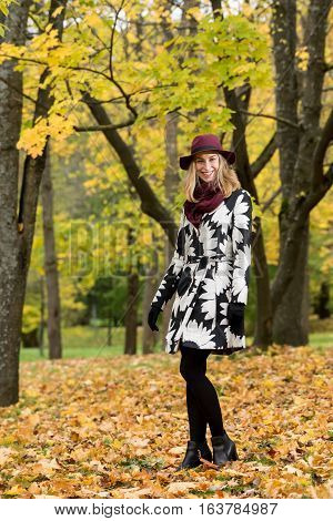 Woman in a floral patterned coat and wine red hat in the park. Happy girl and colorful autumn forest. Portrait of a lady yellow green red and brown leaves background