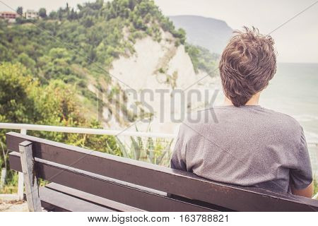 Young Man Sitting On Bench Overlooking Sea