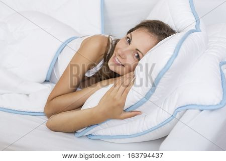 Beautiful young woman lying in bed sleepy and pensive stretching and waking up