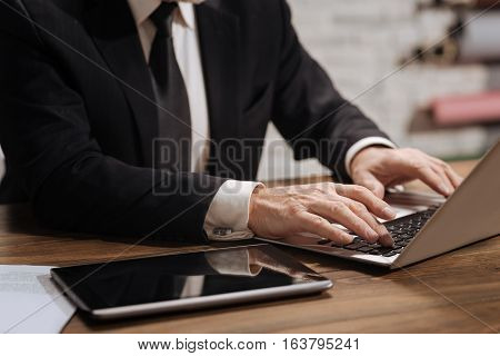Neat and clean. Well dressed focused senior office worker using his computer and typing a current report while sitting at the desk in his office