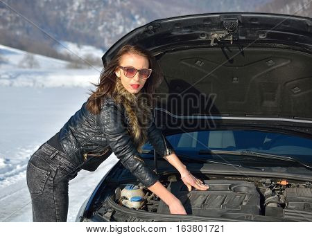 Winter car breakdown - young fashion woman trying to fix the car