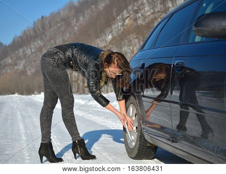 Winter car breakdown - young fashion woman trying to fix the car