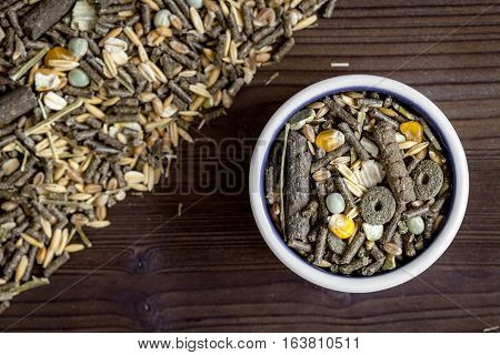 dry food for rodents in bowl on dark wooden background top view.