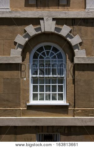 Ornate colonial style radius window with Voussoir stone arch on a historic building in downtown Charleston, South Carolina.