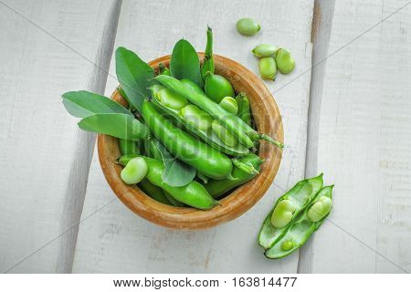 Bowl of podded green broad beans on a wooden table. Healthy organic food. Top view.