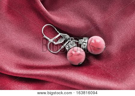 Silver coral earrings on red satin as a background